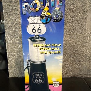 May include: A Route 66 retro gas pump pepper mill and salt shaker. The black and silver design features the Route 66 logo and the text "Retro Gas Pump Pepper Mill/Salt Shaker". The packaging has the text "you can drive forever on Route 66".