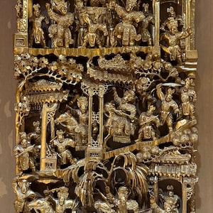 May include: A rectangular gold-colored wood carving featuring intricate relief scenes of figures in traditional attire, including warriors on horseback and architectural structures with tiered roofs, all rendered in a highly detailed, layered style.