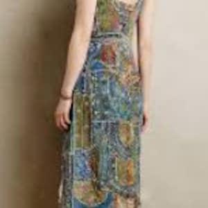 May include: A patterned midi dress in shades of blue, green, and gold. The dress has a sleeveless design and a fitted bodice that flows into a slightly flared skirt. The dress is worn with brown sandals. The pattern has a patchwork style.