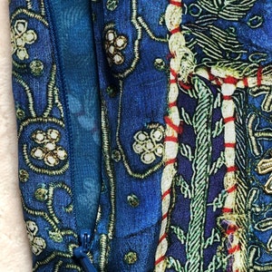 May include: Close-up of a blue patterned fabric with a zipper. The design features floral and geometric motifs in white, green, and red. The fabric has a contrasting blue lining, creating a rich, textured appearance.