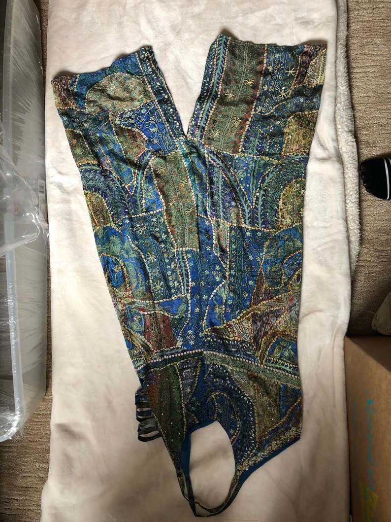 May include: A patchwork jumpsuit in shades of blue, green, and gold, with detailed patterns and embellishments. The halter-style top flows into wide-leg trousers. The fabric looks lightweight, ideal for warmer weather.