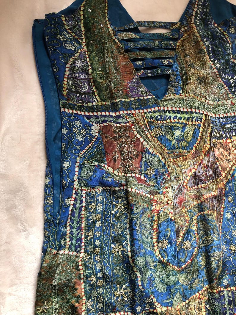 May include: A blue patchwork dress with a V-neck and detailed embroidery. The dress showcases a blend of patterns in blue, green, and brown, with a crisscross design at the neckline. The dress has a side zipper.