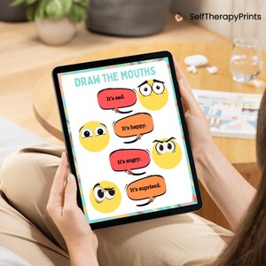 May include: A digital tablet displaying a printable worksheet for drawing mouths on different facial expressions. The worksheet includes four cartoon faces with different eye expressions and the text "Draw the Mouths" at the top. The text below each face reads "It's sad", "It's happy", "It's angry", and "It's surprised".