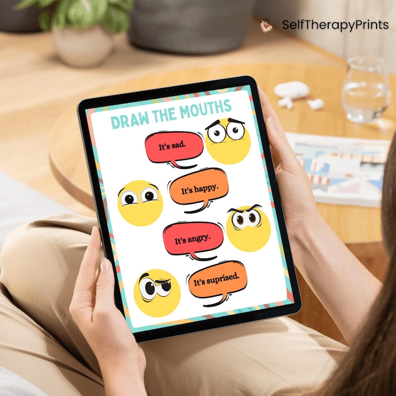 May include: A digital tablet displaying a printable worksheet for drawing mouths on different facial expressions. The worksheet includes four cartoon faces with different eye expressions and the text "Draw the Mouths" at the top. The text below each face reads "It's sad", "It's happy", "It's angry", and "It's surprised".