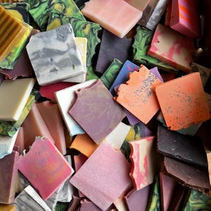 Puede incluir: Una colección de jabones artesanales coloridos de diferentes formas y tamaños. Los jabones están dispuestos en una caja y presentan una variedad de colores, incluyendo verde, rosa, morado, naranja y marrón.