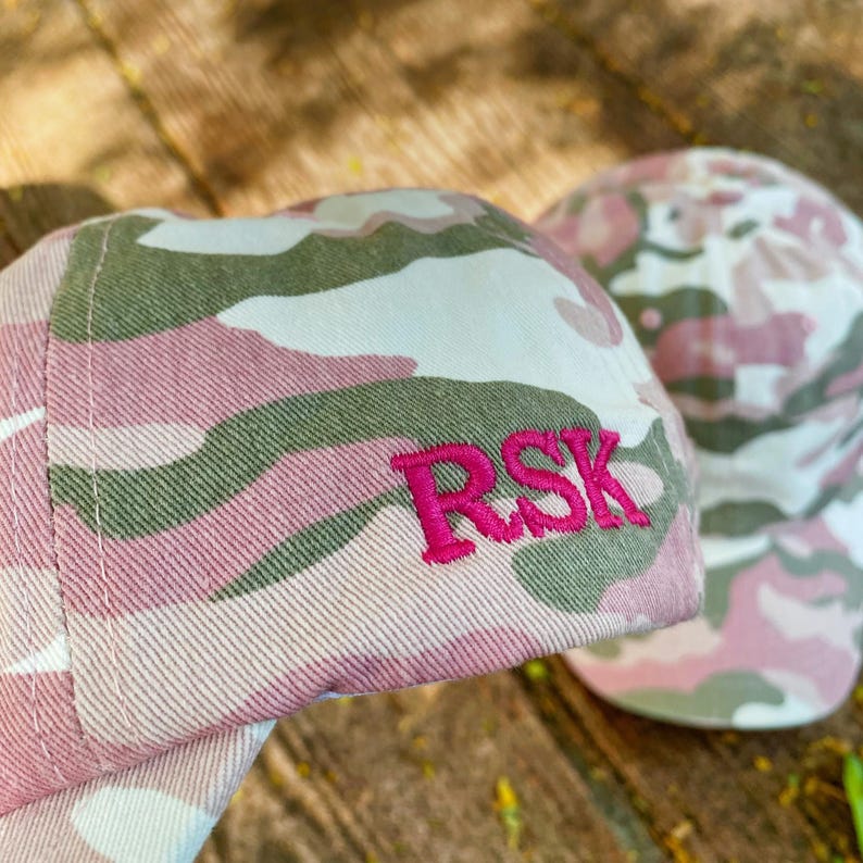 Puede incluir: Gorra de b&eacute;isbol de camuflaje rosa y verde con las iniciales "RSK" bordadas en rosa.