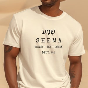 May include: A white t-shirt with the Hebrew word "Shema" and the English translation "Hear - Do - Obey" and the reference "Deut. 6:4" printed on the front.