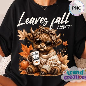 Puede incluir: Una camiseta negra con el gráfico de una vaca highland peluda con gafas de sol y una diadema de leopardo. La vaca lleva un suéter beige y sostiene un vaso de café con la etiqueta Fueled by Chaos. El texto dice Leaves fall I DON'T.