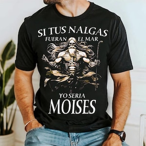 Puede incluir: Una camiseta negra de manga corta con un gráfico de una figura barbuda de pelo largo que sostiene un bastón. El texto superior dice SI TUS NALGAS FUERAN EL MAR y el texto inferior dice YO SERIA MOISES en una fuente serif de color blanco.