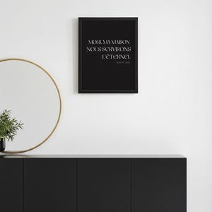 May include: A black framed print with white text that reads "MOI & MA MAISON NOUS SERVIRONS L'ÉTERNEL" above the scripture reference. The print hangs on a white wall above a black cabinet. A gold-framed mirror and a small plant are also visible.