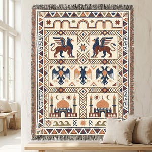 May include: A woven throw blanket featuring a cream background with a multi-colored geometric border. The design includes two winged griffins, three double-headed eagles, and two domed buildings with minarets, accented by stars, suns, and moons.