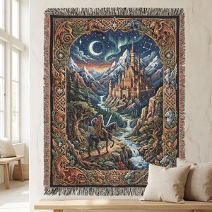 May include: A woven tapestry blanket featuring a fantasy scene with a knight on horseback riding toward a castle in the mountains. The design includes a crescent moon, aurora borealis, and a decorative border with dragon motifs and fringe edges.
