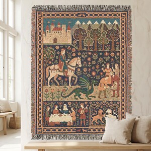 May include: A rectangular woven tapestry throw blanket featuring a medieval scene with a castle, snow-capped mountains, a rider on a white horse, a green dragon, and figures in a garden. The border has a chain-link pattern with fringed edges.