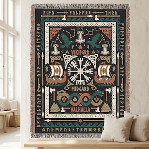 May include: A black woven throw blanket with a Viking theme. The design includes Viking ships, axes, and runes, with the words "Vikingrr", "Midgard", and "Valhalla". The blanket has a fringed edge and is displayed on a wall.