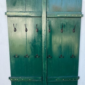 Op de afbeelding: Een groene houten wandbevestigde kapstok met meerdere haken. De kapstok is gemaakt van twee panelen met een rustieke uitstraling en heeft een donkergroene afwerking.