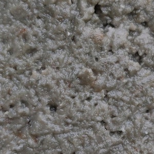 Puede incluir: Primer plano de una sustancia gris, texturizada y viscosa. La sustancia tiene una textura ligeramente granulada y parece estar hecha de pequeñas partículas irregulares. La imagen se toma desde una perspectiva ligeramente inclinada, dando al espectador una sensación de profundidad.