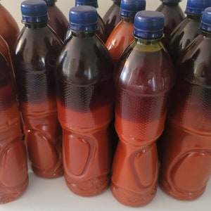 Könnte beinhalten: Eine Gruppe von 10 Plastikflaschen, gefüllt mit einer rot-orangenen Flüssigkeit. Die Flaschen haben blaue Verschlüsse und sind in einem Halbkreis auf einer weißen Oberfläche angeordnet.