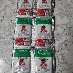 May include: Six individual packets of Gino Tomato Mix. Each packet is silver with a green label that says "Tomato Mix" and features a cartoon character with a tomato. The label also says "Thick, Red & Rich in Vitamins A & C".