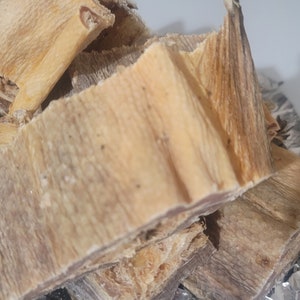 May include: A pile of dried fish strips, light brown in color, with a slightly rough texture. The fish strips are stacked on top of each other, and some are slightly curled.