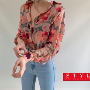May include: A floral print blouse in pink, red, and purple, with long sleeves, paired with light blue jeans. The image includes the text "STYLE SAVVYSTUDIOART" in a red rectangle. The blouse is sheer.