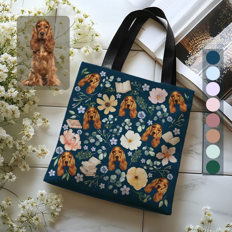 May include: A dark blue tote bag with a floral pattern featuring a repeating image of a brown and white cocker spaniel dog. The bag has black handles.