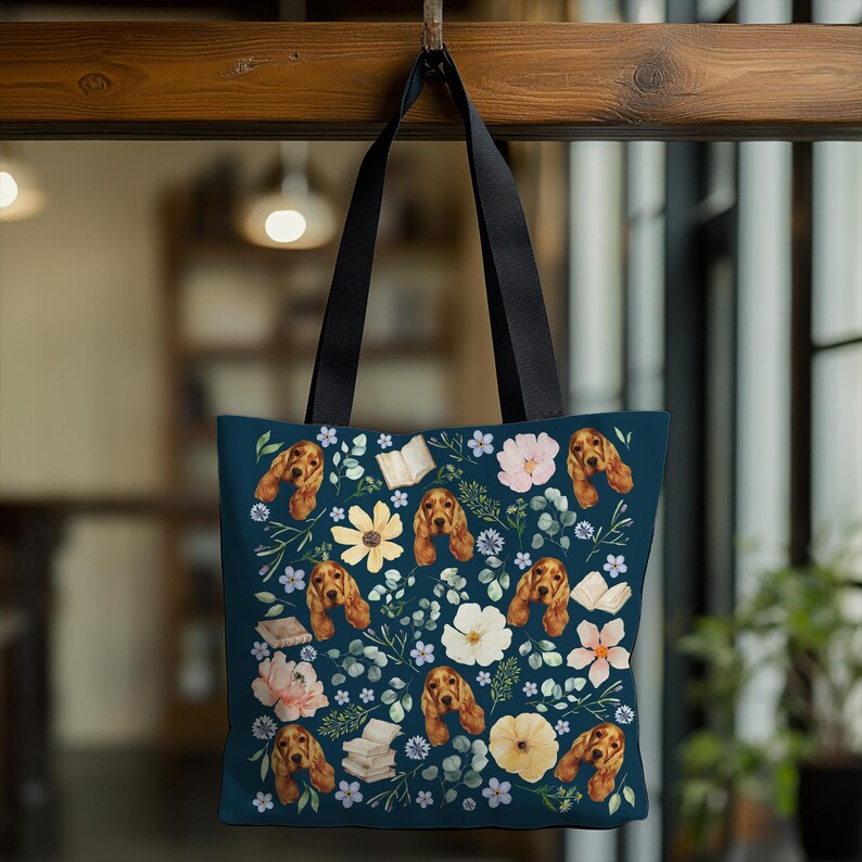 May include: A blue tote bag with a floral pattern featuring a dog's face and a book. The flowers are in shades of pink, yellow, and white.