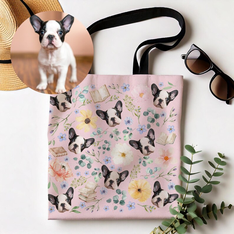 May include: A pink tote bag featuring a repeating pattern of a French bulldog's face, flowers, and books. The bag has black handles.