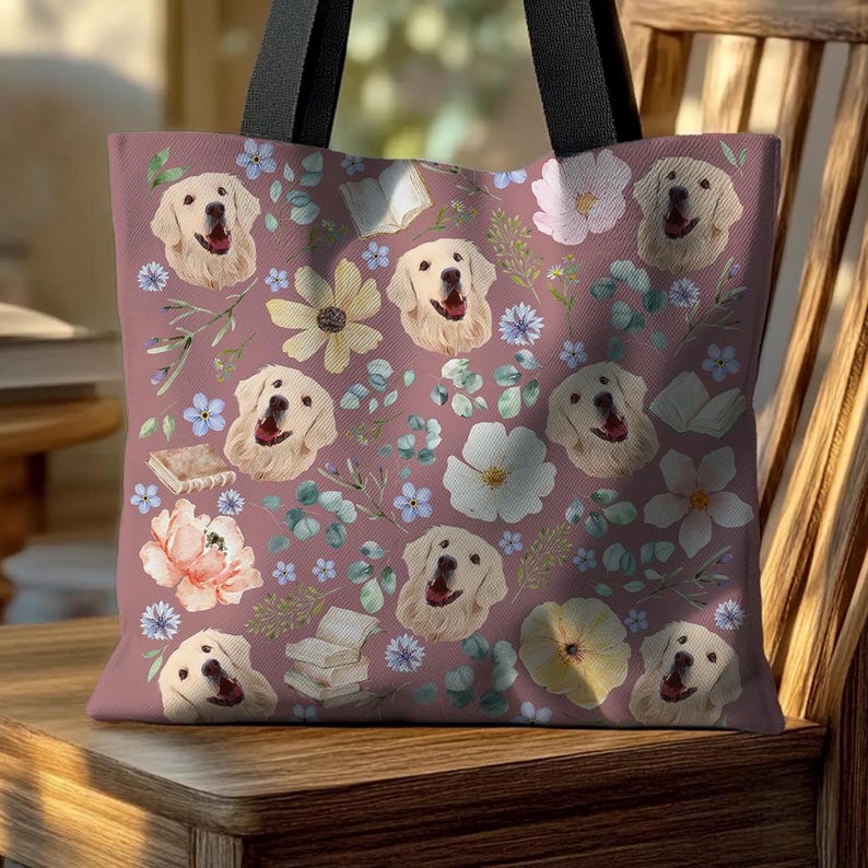 May include: A pink tote bag featuring a floral pattern and repeated images of golden retrievers. The flowers are in shades of yellow, white, and pink. The bag has black handles.