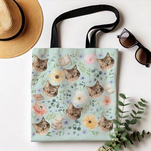 May include: A light blue tote bag with a repeating pattern of brown tabby cats, flowers, and books. The bag has black straps.