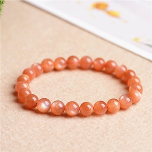 Könnte beinhalten: Ein Armband aus orangefarbenen Sunstone-Perlen. Die Perlen sind rund und haben eine schimmernde, irisierende Oberfläche.