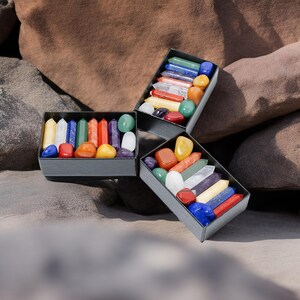 May include: A set of colorful tumbled stones and points in a black box. The stones are arranged in rows by color, with each row representing a different chakra.