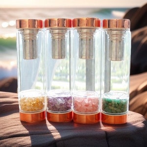 Puede incluir: Cuatro botellas de agua de vidrio transparente con tapas y bases de color cobre. Cada botella contiene piedras pequeñas de diferentes colores: amarillo, morado, rosa y verde. Las botellas tienen un infusor incorporado.