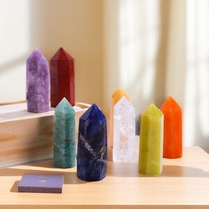 May include: Seven crystal points in various colours, including purple, red, green, blue, clear, yellow, and orange, are arranged on a wooden surface. The crystals are all pointed and have a smooth, polished finish.