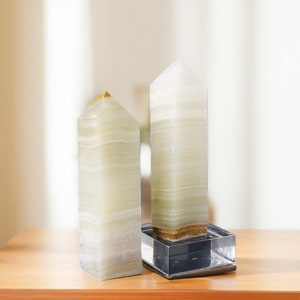 Könnte beinhalten: Zwei grüne und weiße gestreifte Onyx-Kristalltürme auf einer Holzoberfläche. Der Turm rechts steht auf einem klaren Glassockel.