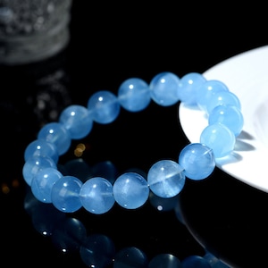 May include: A light blue gemstone bracelet with round beads. The bracelet is made of natural aquamarine stones.