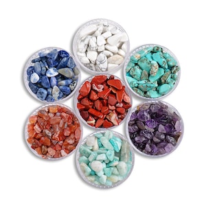 May include: Seven clear plastic containers filled with various tumbled gemstones. The stones are in shades of white, blue, red, orange, turquoise, purple, and green. The containers are arranged in a circular pattern against a white background.
