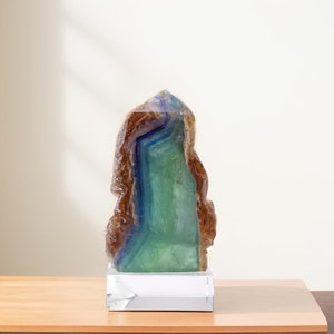 以下が含まれることがあります： 透明なガラスの台座の上に置かれた、大きく、緑色、青色、茶色のクリスタル。クリスタルはユニークな自然な形をしており、美しい装飾品です。