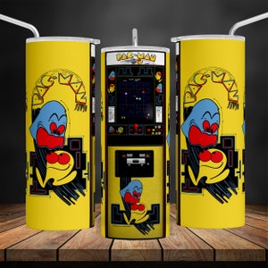May include: A yellow tumbler with a Pac-Man design. The design features Pac-Man and a ghost on a black and yellow background. The text "PAC-MAN" is printed in white on the tumbler.