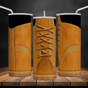 May include: A brown leather boot with a black top and laces. The boot is wrapped around a stainless steel tumbler.