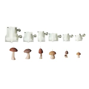 May include: A collection of six translucent white silicone molds for casting mushroom shapes, each secured with metal binder clips, displayed alongside six finished brown and beige mushroom-shaped candles of varying sizes and cap textures.
