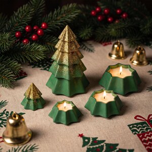 Könnte beinhalten: Ein Set aus grünen und gold glitzernden weihnachtsbaumförmigen Kerzen und sternförmigen Teelichtern mit brennenden Dochten. Das Set enthält einen großen Baum, einen kleinen Baum, drei sternförmige Kerzenhalter sowie zwei goldene Glocken.