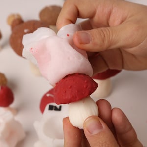 May include: A flexible silicone mold for casting mushroom shapes, featuring a white translucent top section and a red textured bottom section. The mold is designed to create detailed mushroom caps and stems, with multiple units visible in the background.