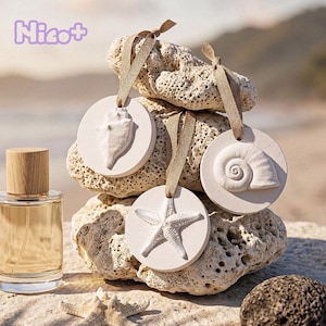 Könnte beinhalten: Eine Parfümflasche mit Holzverschluss und klarem Glaskörper steht neben einem Stapel weißer, kreisförmiger Ornamente. Jedes Ornament zeigt ein anderes geprägtes Muscheldesign und ein beiges Band zum Aufhängen. Das Wort "Nicot+" befindet sich oben links.