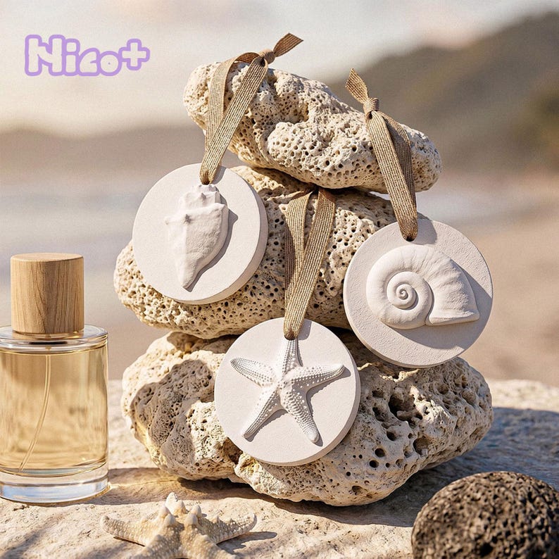 Op de afbeelding: Een parfumfles met een houten dop en een heldere glazen body staat naast een stapel witte, cirkelvormige ornamenten. Elk ornament heeft een ander reli&euml;f schelpmotief en een bruin lint om op te hangen. Het woord "Nicot+" staat linksboven.