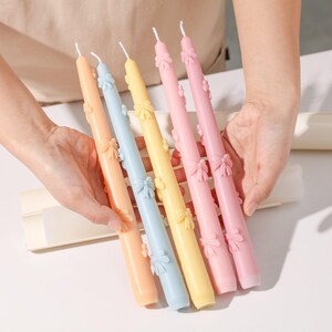 A vibrant display showcasing Ribbon Bow Taper Candles in various colors, each adorned with an intricate bow design.