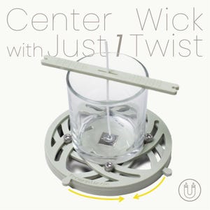 Puede incluir: Una herramienta para hacer velas con un tarro de vidrio transparente, una mecha y un dispositivo de centrado verde claro. La base es verde claro con un diseño circular y el texto "Center Wick with Just 1 Twist".