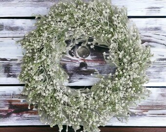 May include: A white baby's breath wreath on a whitewashed wood background.