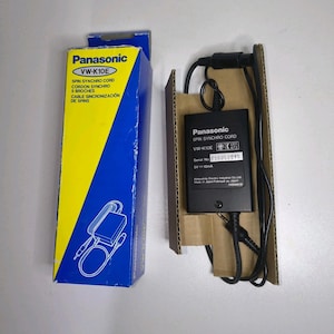 May include: A Panasonic VW-K10E Spin Synchro Cord, with its original box. The box is blue and yellow, with the product name and a diagram. The cord is black, with a black rectangular component and a serial number.