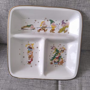 Peut inclure: Plat de service blanc divisé avec bordure dorée, représentant les Sept Nains de Blanche-Neige. Le plat comporte trois sections et est décoré avec les nains et des étoiles dorées. Un charmant objet de collection.