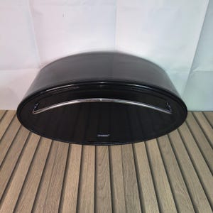 May include: A black, oval bread bin with a curved lid and a silver handle. The bread bin has a glossy finish and a simple design. The bin is on a wooden surface. The dimensions are approximately 40cm x 25cm x 15cm.